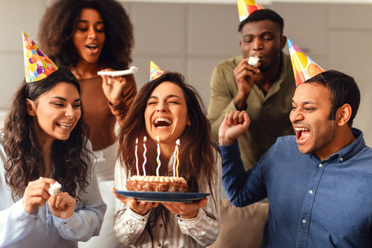 A group of friends celebrating a half birthday and blowing out the candles on a cake 