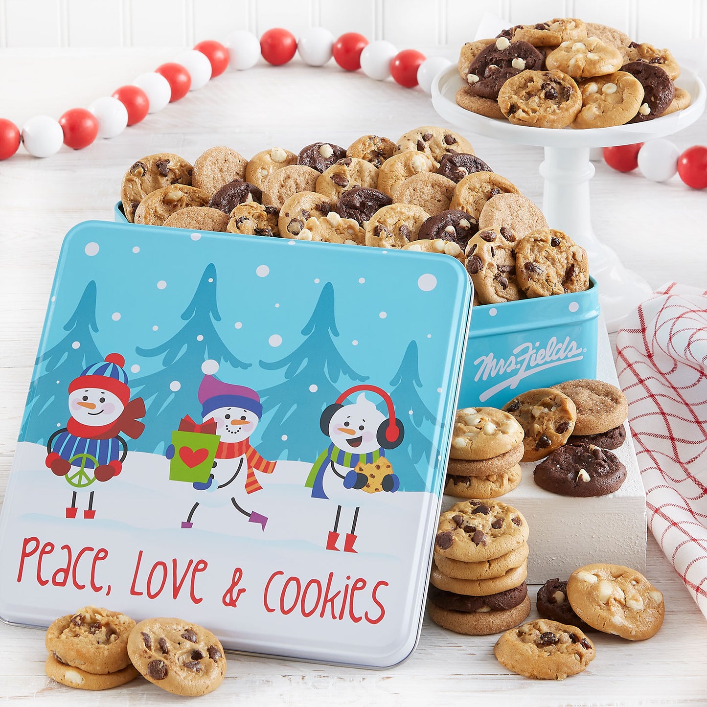 Peace, Love, and Cookies sentiment on a gift tin with snowman friends as decorations. This tin is filled with an assortment of Nibblers®