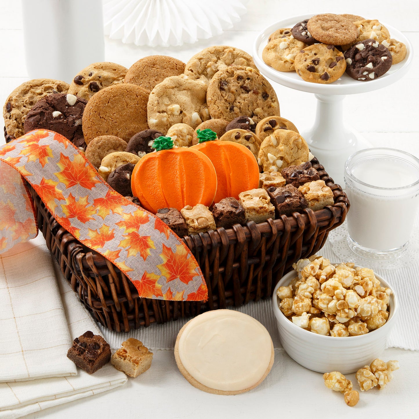 Brown basket with fall ribbon decorated in orange leaves. This basket is filled with an assortment of Nibblers® , brownie bites and frosted round and pumpkin shaped cookies. 