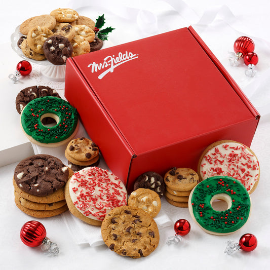 A classic red Mrs. Fields gift box with an assortment of original cookies, Nibblers®, two frosted wreaths with sprinkles, and two peppermint round cookies with sprinkles.