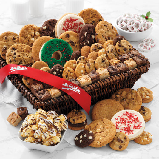 A brown basket filled with an assortment of original cookies, Nibblers®, brownie bites, yogurt-covered pretzels, two peppermint cookies with sprinkles, one frosted wreath cookie with sprinkles, and chocolate drizzled popcorn and decorated with a red Mrs. Fields' ribbon.