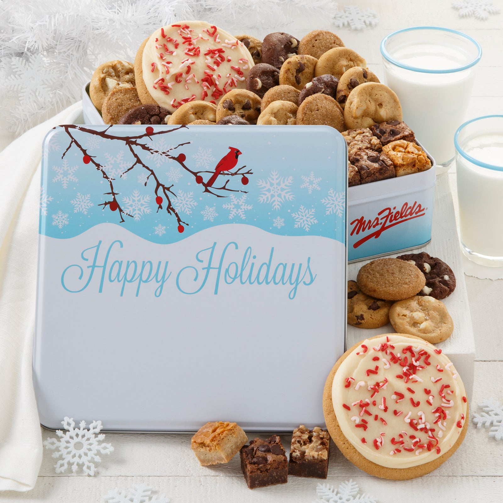 An outdoor winter scene with a red cardinal as decoration on a gift tin that is filled with an assortment of Nibblers®, brownie bites, and two frosted peppermint cookies with sprinkles