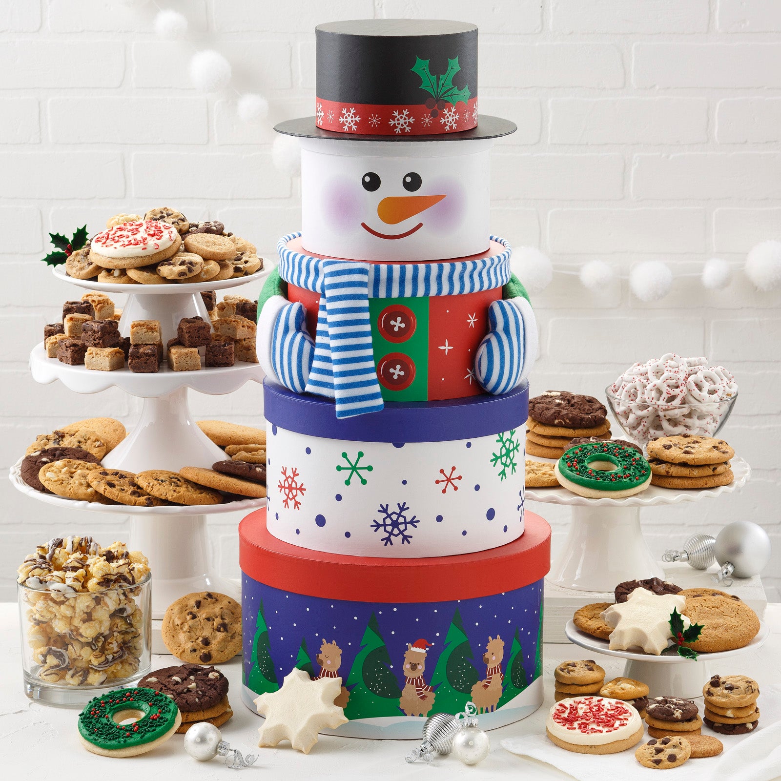 A festive five-tier snowman tower surrounded by an assortment of Nibblers®, original cookies, two frosted wreath cookies with sprinkles, two frosted peppermint cookies with sprinkles, two frosted snowflake cookies,  holiday popcorn, and yogurt-covered pretzels. 