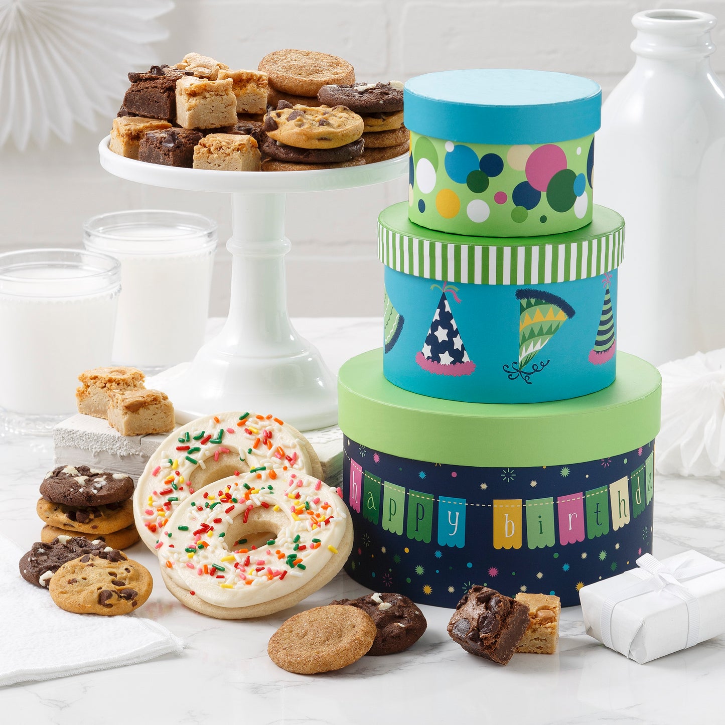 Birthday gift tower surrounded by an assortment of nibblers, brownie bites and frosted cookies 