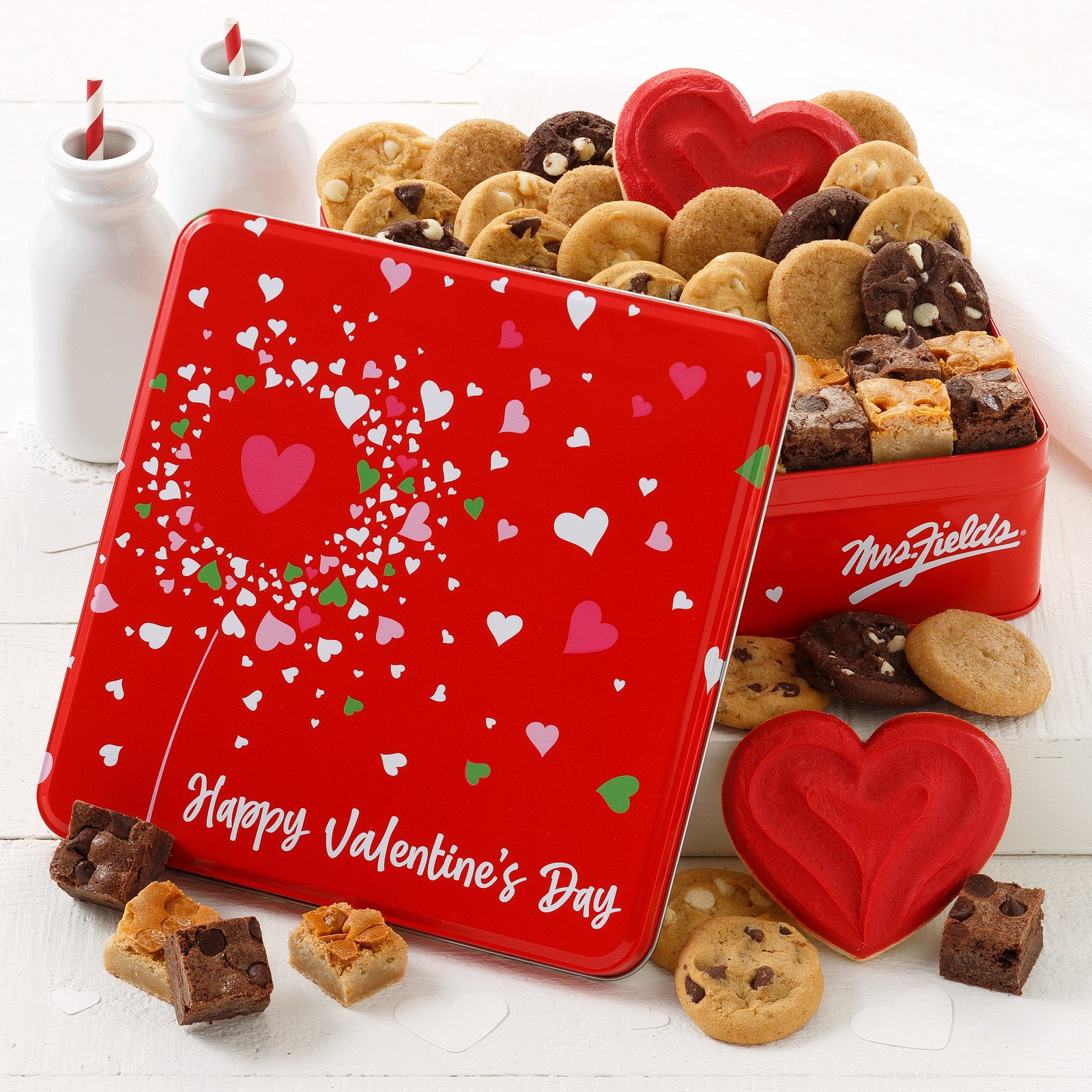 A red with hearts Valentine's Day tin filled with an assortment of nibblers, brownie bites, and frosted heart cookies