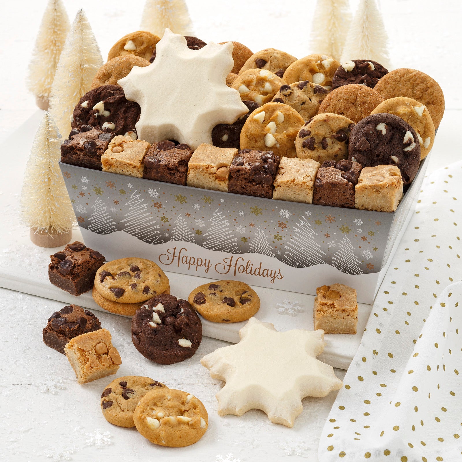 A Happy Holidays crate decorated with snowy forest of silver, white and gold and filled with an assortment of Nibblers®, brownie bites and two frosted snowflake cookies.