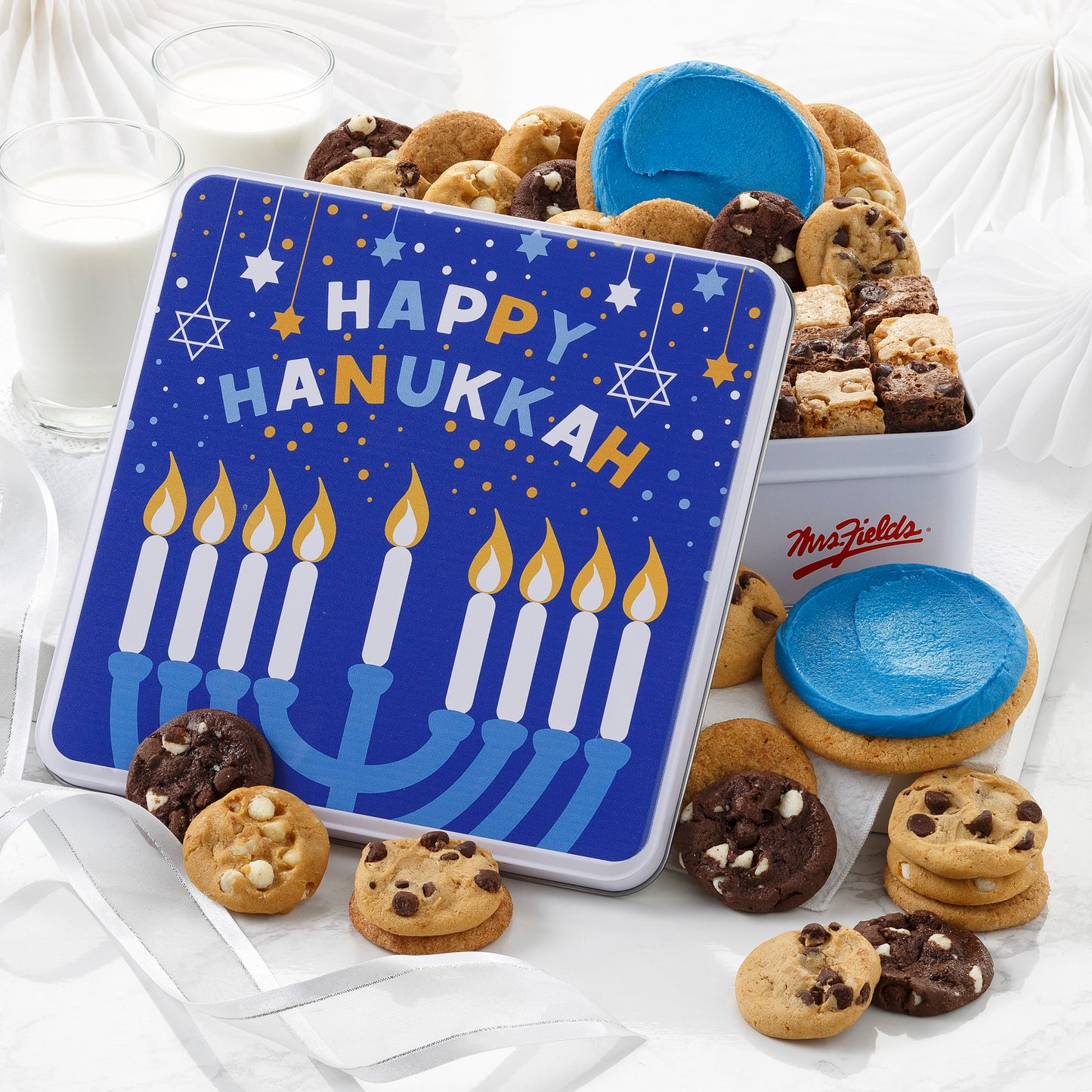 A blue and white Happy Hanukkah gift tin filled with an assortment of Nibblers®, brownie bites, and two frosted round cookies