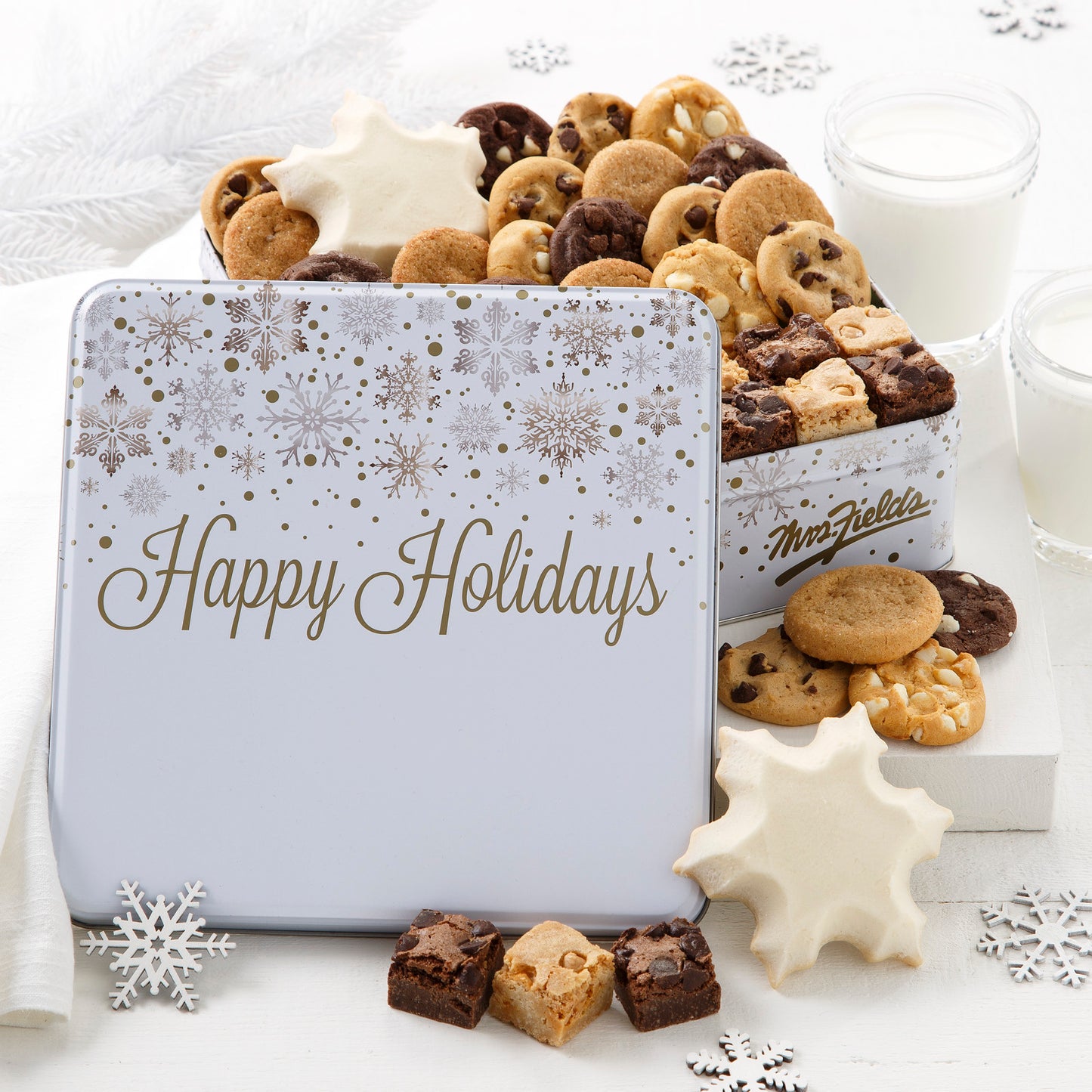 A happy holiday white and gold tin decorated with snowflakes and filled with an assortment of Nibblers®, brownie bites, and two frosted snowflake cookies.