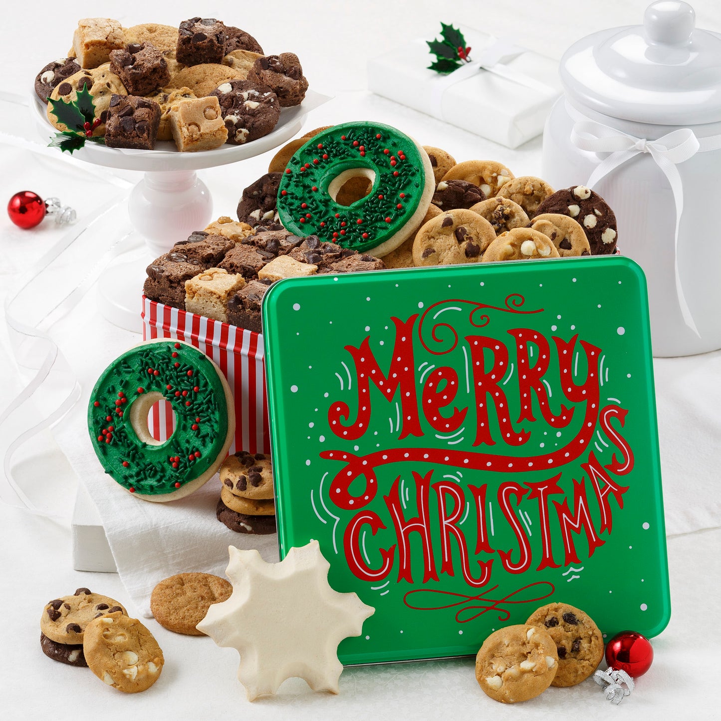 A green Merry Christmas tin decorated with red words and falling snow. Includes a variety of 36 assorted Nibblers® bite-sized cookies, 18 brownie bites, 2 frosted holiday wreath cookies and 1 frosted snowflake cookies.