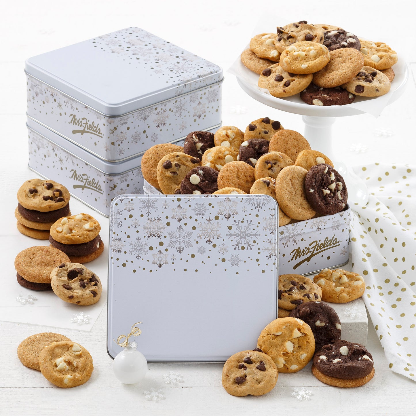 Three white holiday tins decorated with gold and silver snowflakes and filled with an assortment of Nibblers®