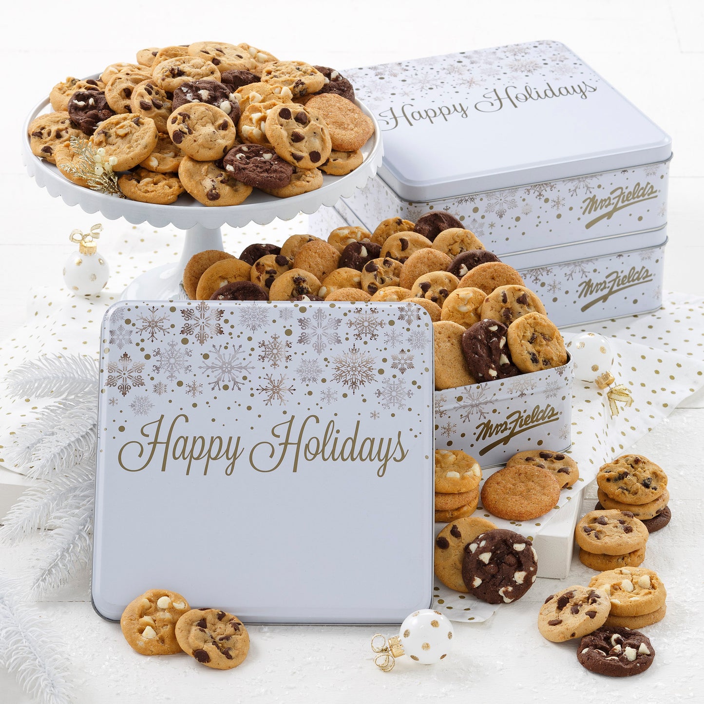 Three Happy Holiday white tins decorated with gold and silver snowflakes and filled with an assortment of Nibblers®.