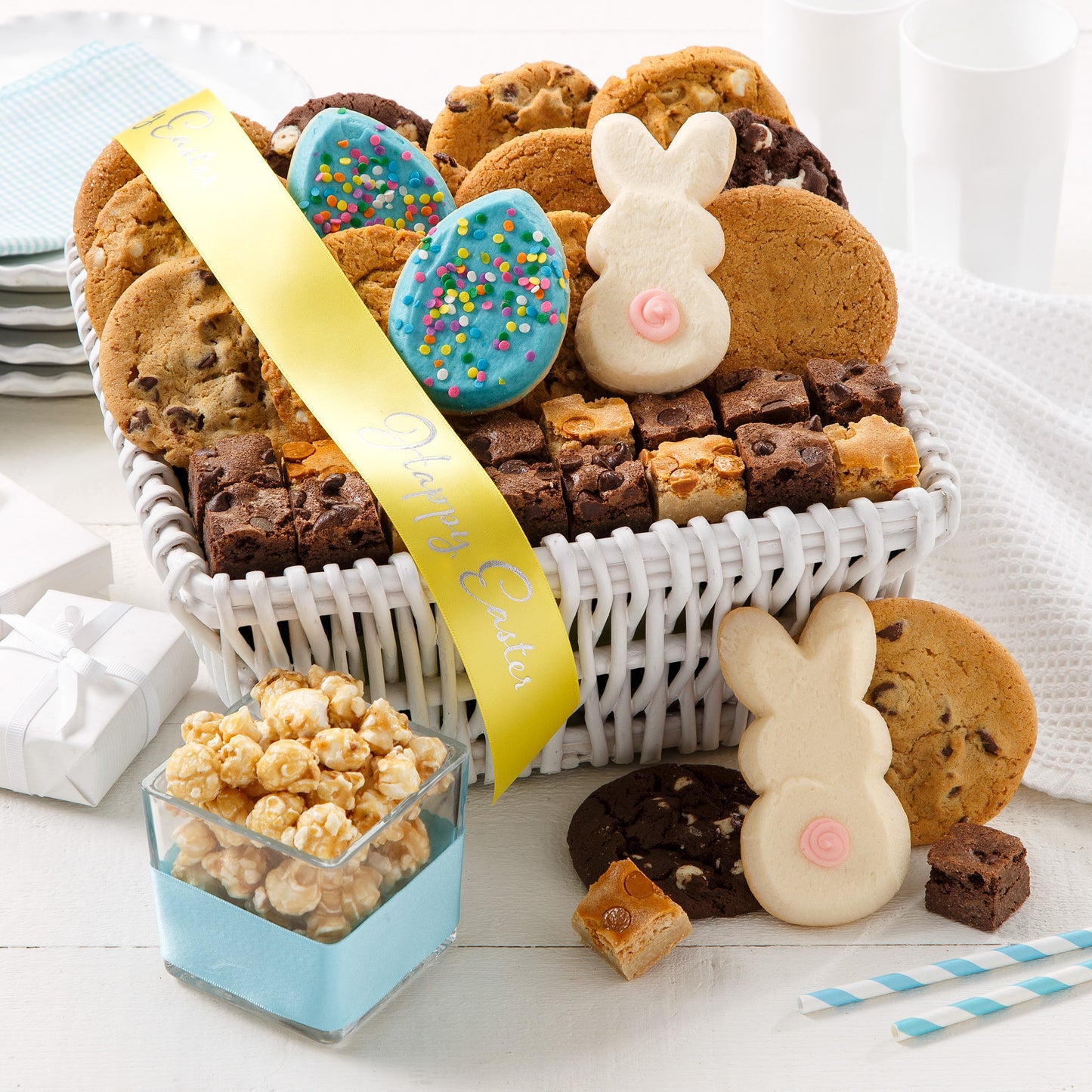 A white gift basket with a yellow Happy Easter ribbon filled with an assortment of original cookies, frosted cookies, logo cookies, and popcorn