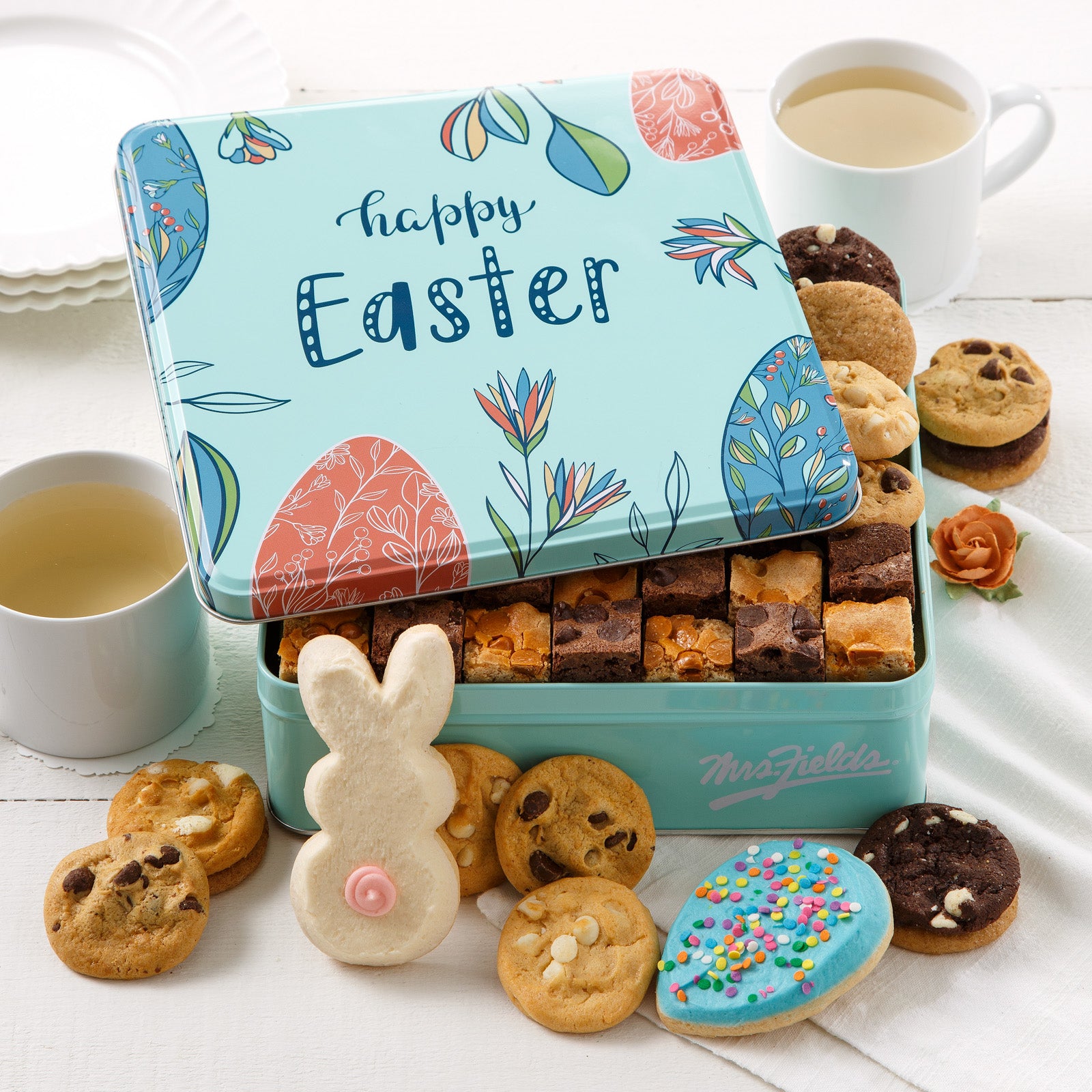 A light blue Easter themed gift tin with a Happy Easter sentiment and filled with an assortment of nibblers, brownie bites, a frosted egg cookie and frosted bunny cookie